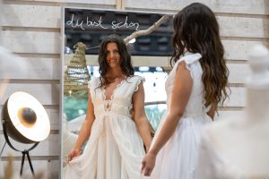 Junge, dunkelhaarige Frau steht im Brautkleid bei der TrauZeit 2022 vor einem Spiegel